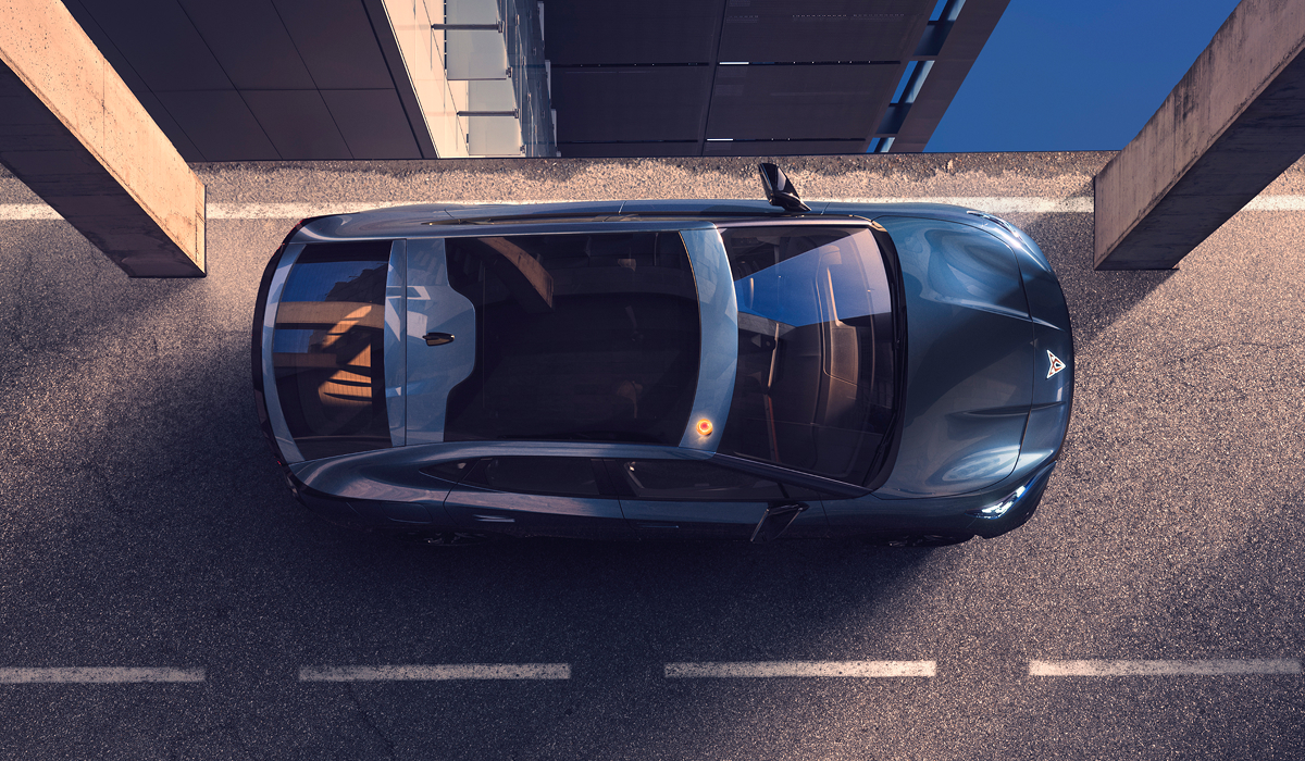 Vogelperspektive auf einen CUPRA Tavascan mit Panoramadach zwischen Betonpfeilern, Reflexion der Architektur auf dem Fahrzeugdach